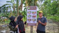 Mahasiswa Kukerta MBKM UNRI berfoto di depan lahan yang terdapat informasi tanaman yang sudah mereka tanam. (doc. Kukerta MBKM UNRI)