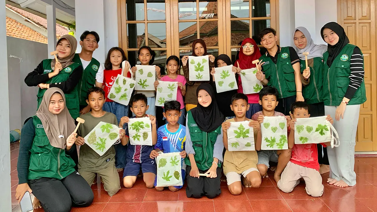 Mahasiswa KKM 55 UNIBA berpose bersama anak-anak Desa Jatimulya sambil memamerkan totebag hasil pelatihan ecoprint berbahan daun dan bunga lokal. (doc. KKM 55 UNIBA)
