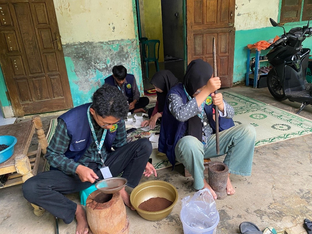 Mahasiswa KKN 251 sedang melakukan penumbukan biji kopi dengan lesung/lumpang dan alu. (doc. KKN 251 UNS)