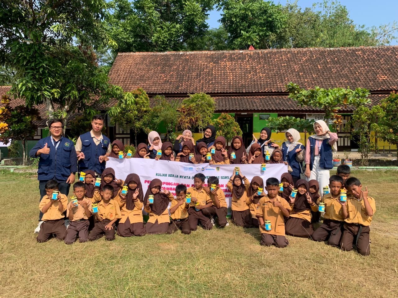 Mahasiswa KKN UNS 107 berpose bersama seluruh siswa SDN 2 Tambakan dengan kreasi Minions hasil karya mereka, menandai keseruan dan keberhasilan kegiatan edukasi 5R. (doc. KKN 107 UNS)