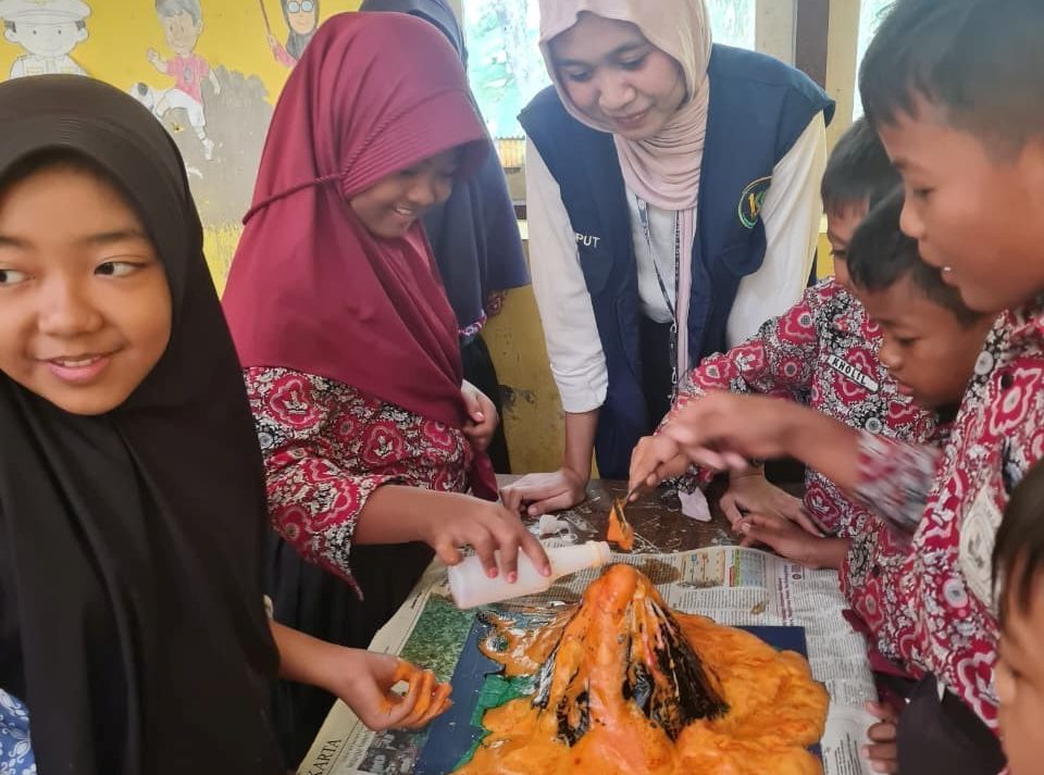 Siswa SDN 2 Tambakan antusias menyaksikan ledakan miniatur gunung berapi dan berdiskusi dengan mahasiswa KKN, tampak fokus dan seru mengikuti eksperimen. (dok. KKN 107 UNS)