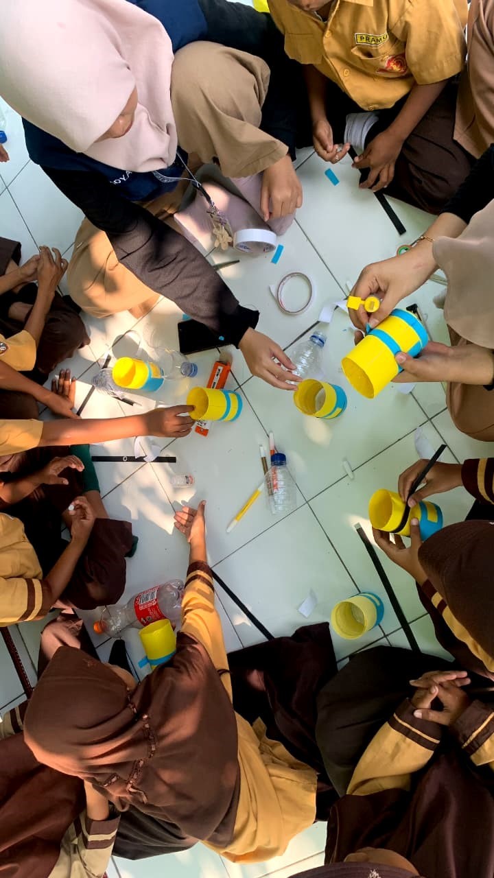 Siswa SDN 2 Tambakan fokus mewarnai dan menempel kertas untuk membuat baju dungaree Minions dari botol bekas, sambil belajar konsep 5R melalui praktik kreatif. (doc. KKN 107 UNS)