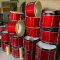Tumpukan bass drum merah siap dikirim ke berbagai sekolah dan komunitas marching band. Peralatan baru ini jadi penunjang utama performa tim perkusi. (doc. pabrikalatdrumband.com)