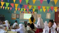 Mahasiswa tengah membimbing siswa sekolah dasar dalam kegiatan belajar interaktif di kelas yang penuh warna dan semangat belajar. (doc. pribadi)