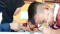 Ilustrasi seorang guru dengan sabar membimbing siswa sekolah dasar dalam proses belajar menulis di kelas. (doc. pribadi)