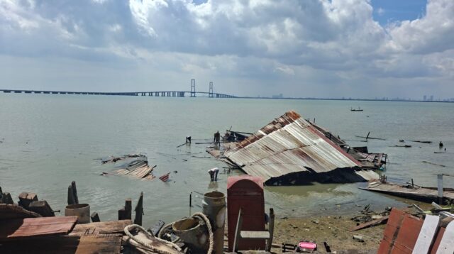 Dermaga Rindu di Kecamatan Labang, Bangkalan, tampak roboh dan tercebur ke laut setelah diterjang angin kencang dan hujan deras. Sejumlah warga terlihat memeriksa sisa bangunan yang rusak dengan latar Jembatan Suramadu di kejauhan. (doc. pribadi)