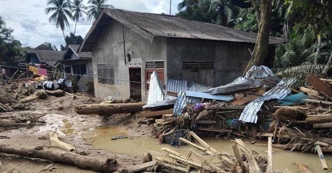Material kayu, lumpur, dan puing bangunan menumpuk di sekitar rumah warga setelah banjir bandang menerjang permukiman di Sumatera pada Desember 2025. (doc. ist)