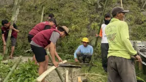 Mahasiswa KKN-PPM UMBY Kelompok 15 bersama warga Dusun Ngepoh Kidul bergotong royong menyiapkan rangka bambu untuk pemasangan jaring penutup talang air, Minggu (8/2/2026). (doc. pribadi)