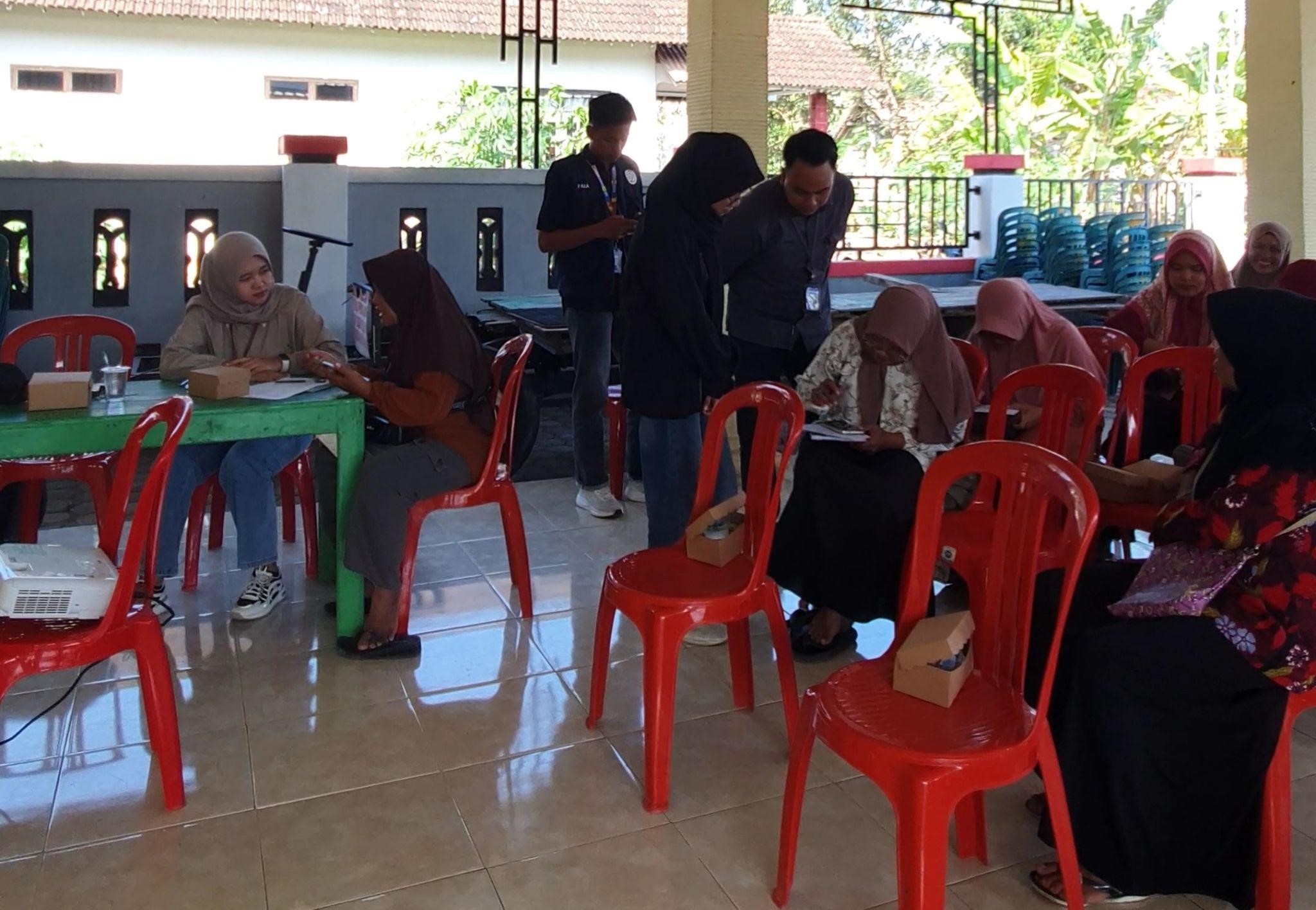 Mahasiswa KKN 195 UNS bersama pegawai Bank BRI Pacitan memberikan pendampingan kepada pelaku UMKM Desa Hadiluwih dalam proses pendaftaran QRIS di Balai Dusun Gareng Kidul, Desa Hadiluwih. (Dok. Pribadi/KKN 195 UNS)