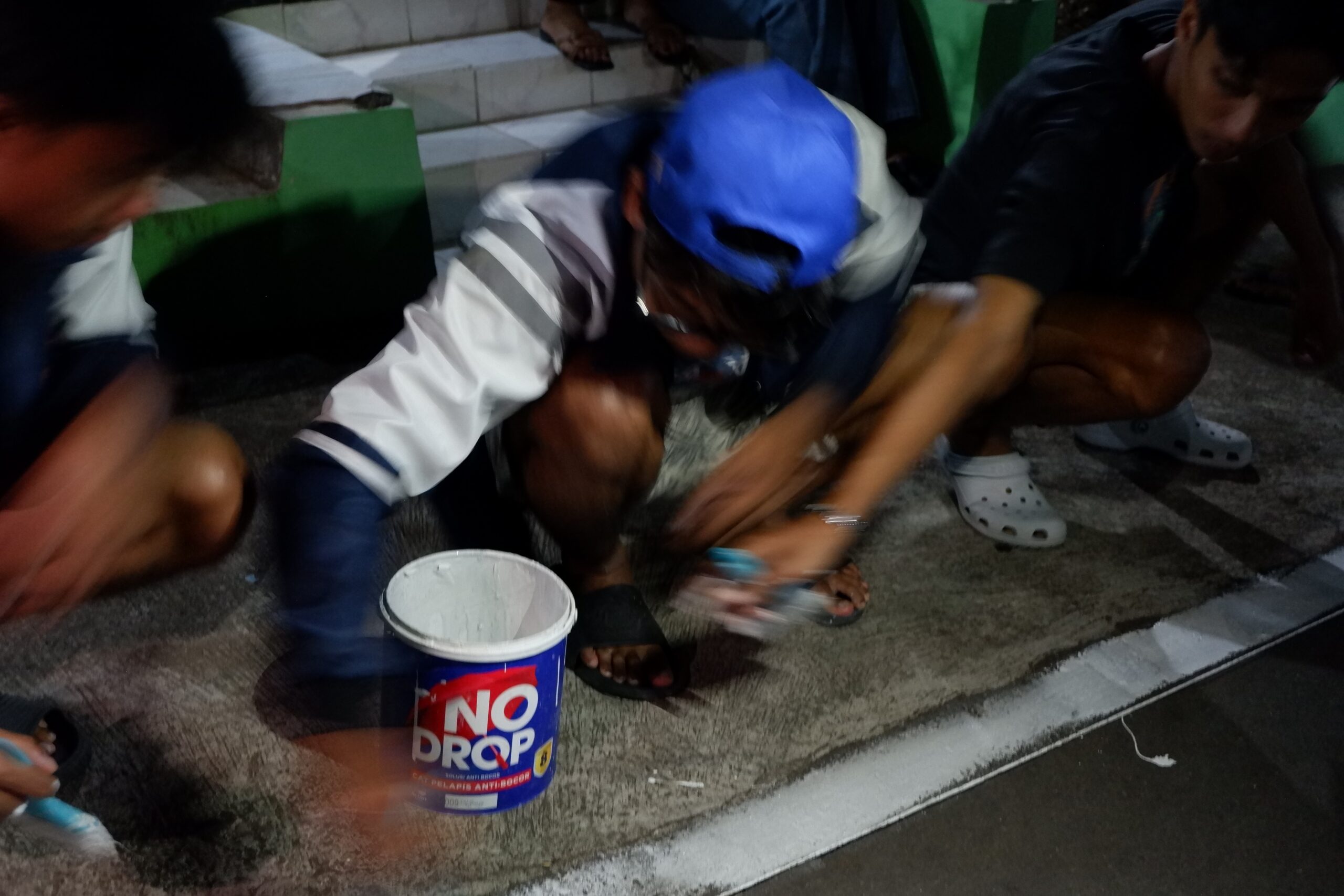 Mahasiswa KKN Undip dan anggota Karang Taruna Jirapan bergotong royong mengecat jalan menggunakan cat pelapis anti bocor. (Dok. Pribadi/Mahasiswa KKN Undip)